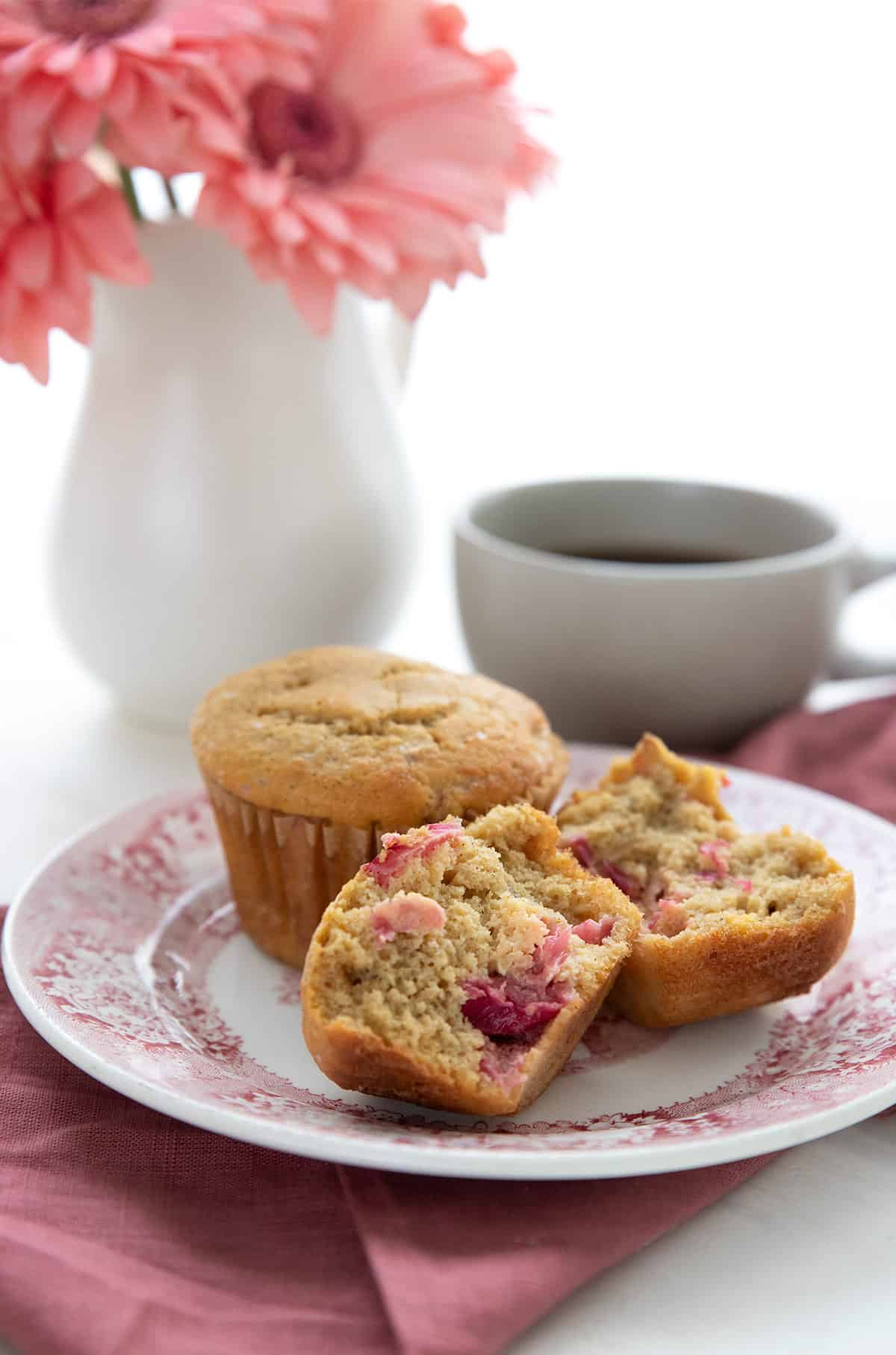 Two keto rhubarb muffins on a red patterned plate, with one broken open to show the inside.