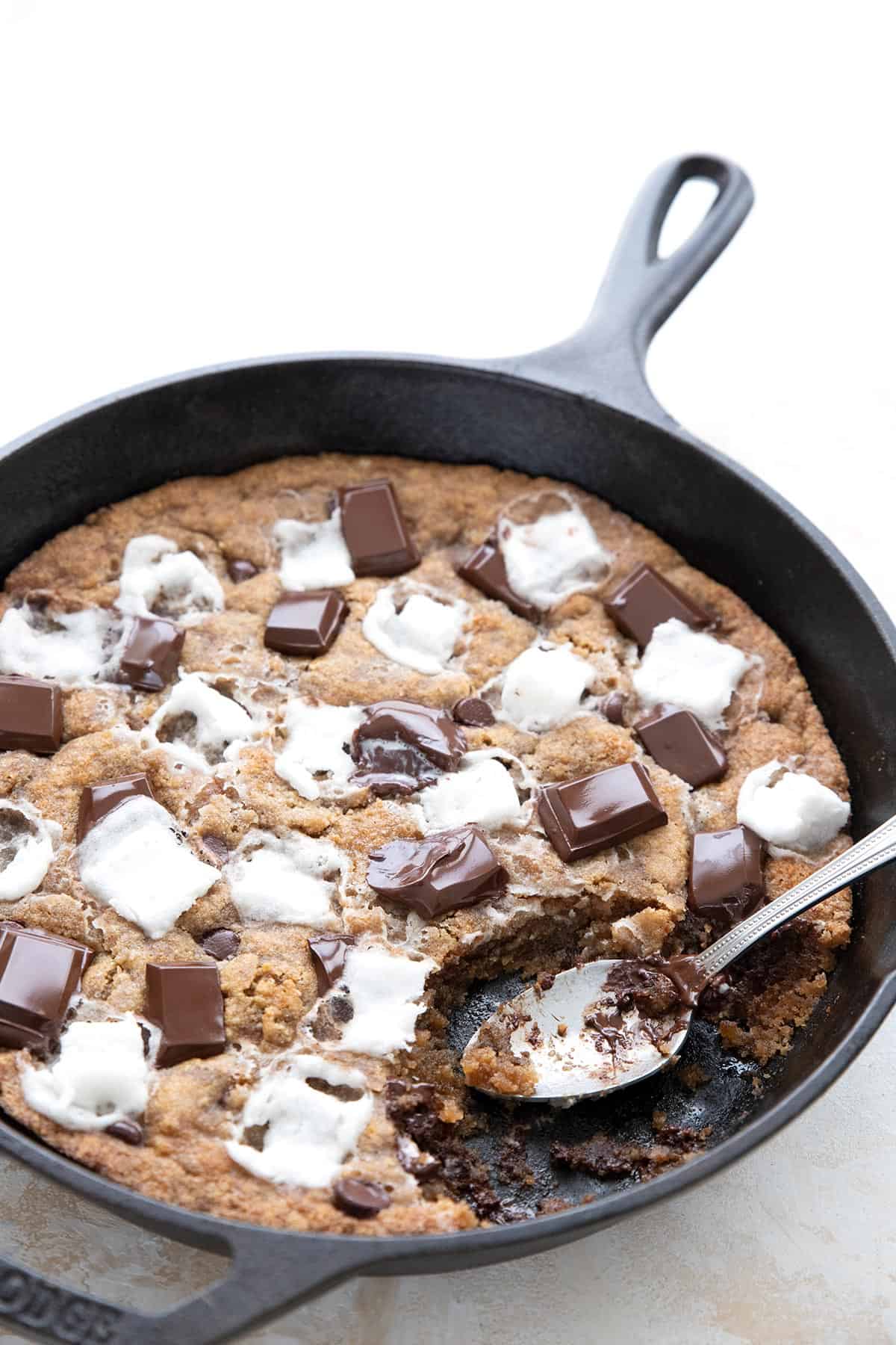 A cast iron skillet on a white table, filled with gooey keto smores cookie.