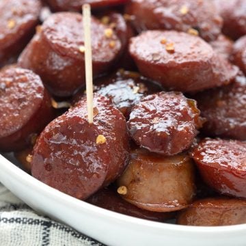 Close up shot of kielbasa bites in a white oval dish over a white and black cloth.