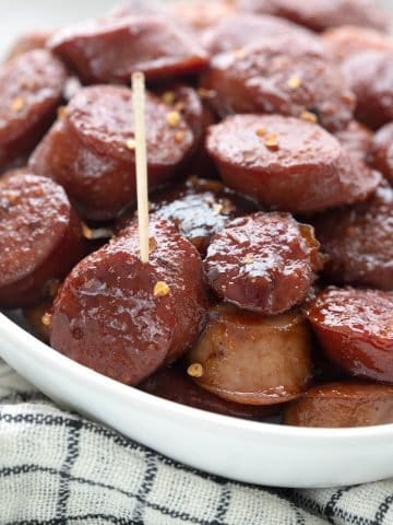 Close up shot of kielbasa bites in a white oval dish over a white and black cloth.