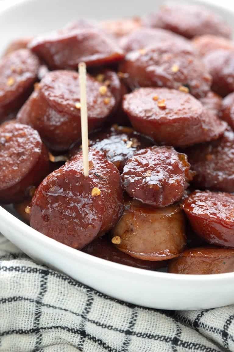 Close up shot of kielbasa bites in a white oval dish over a white and black cloth.