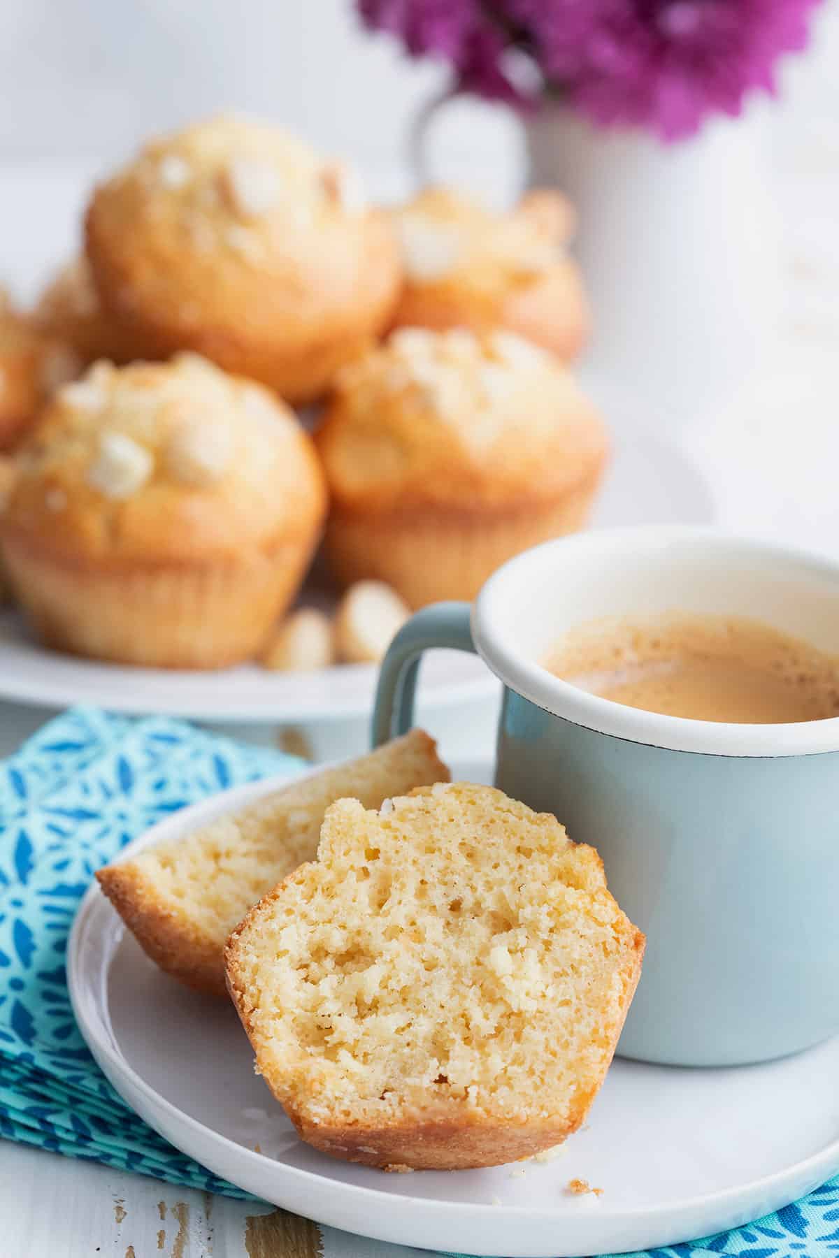 A keto macadamia nut muffin cut open on a white plate with a small cup of coffee.