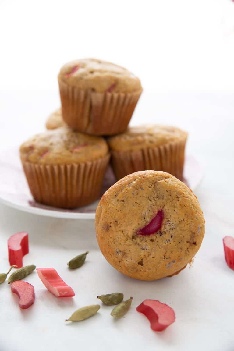 A keto rhubarb muffin with a slice of rhubarb on top, and a plate of more muffins in the background.