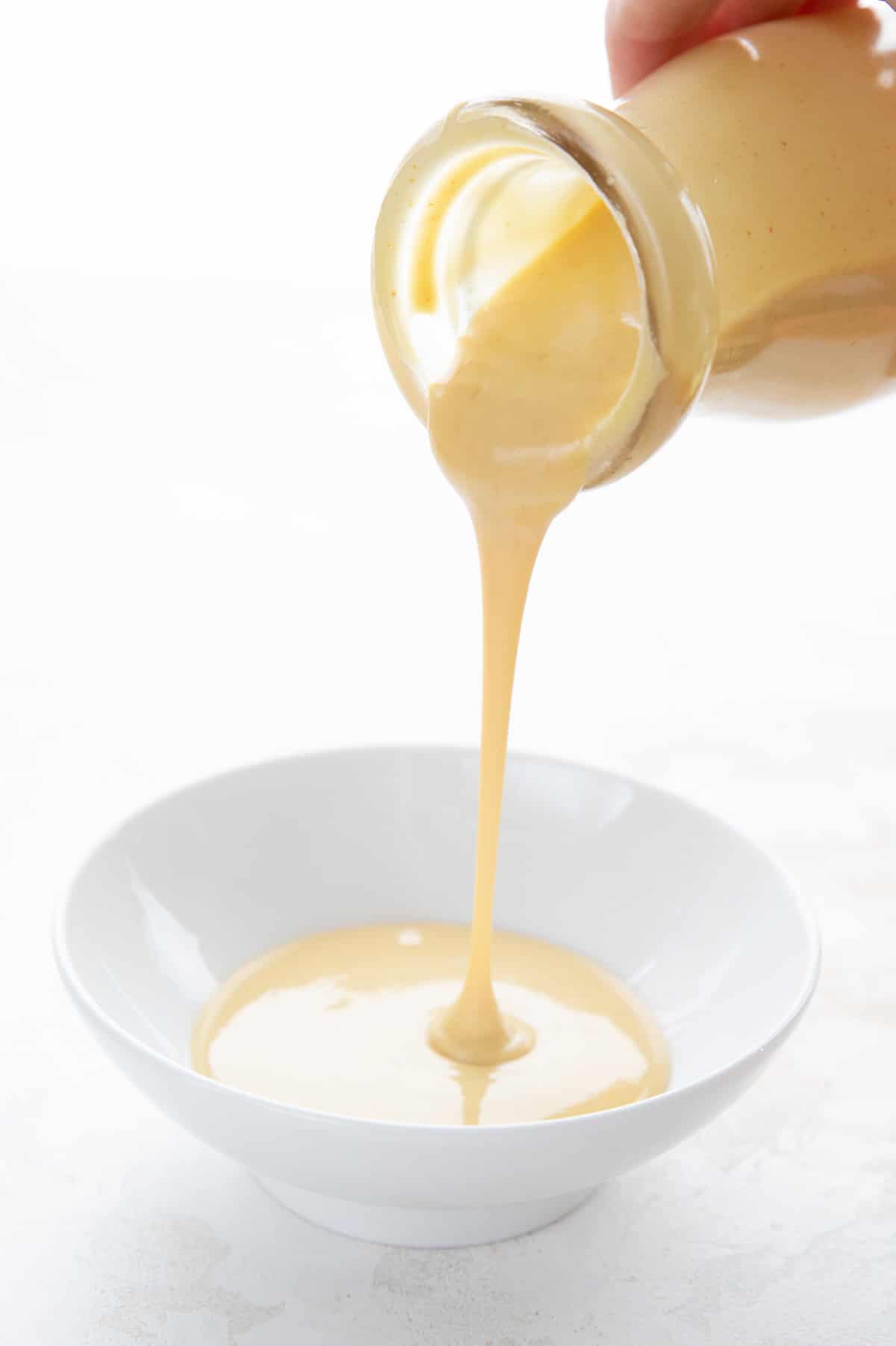 Sugar Free Honey Mustard sauce pouring out of a glass bottle into a white dish.