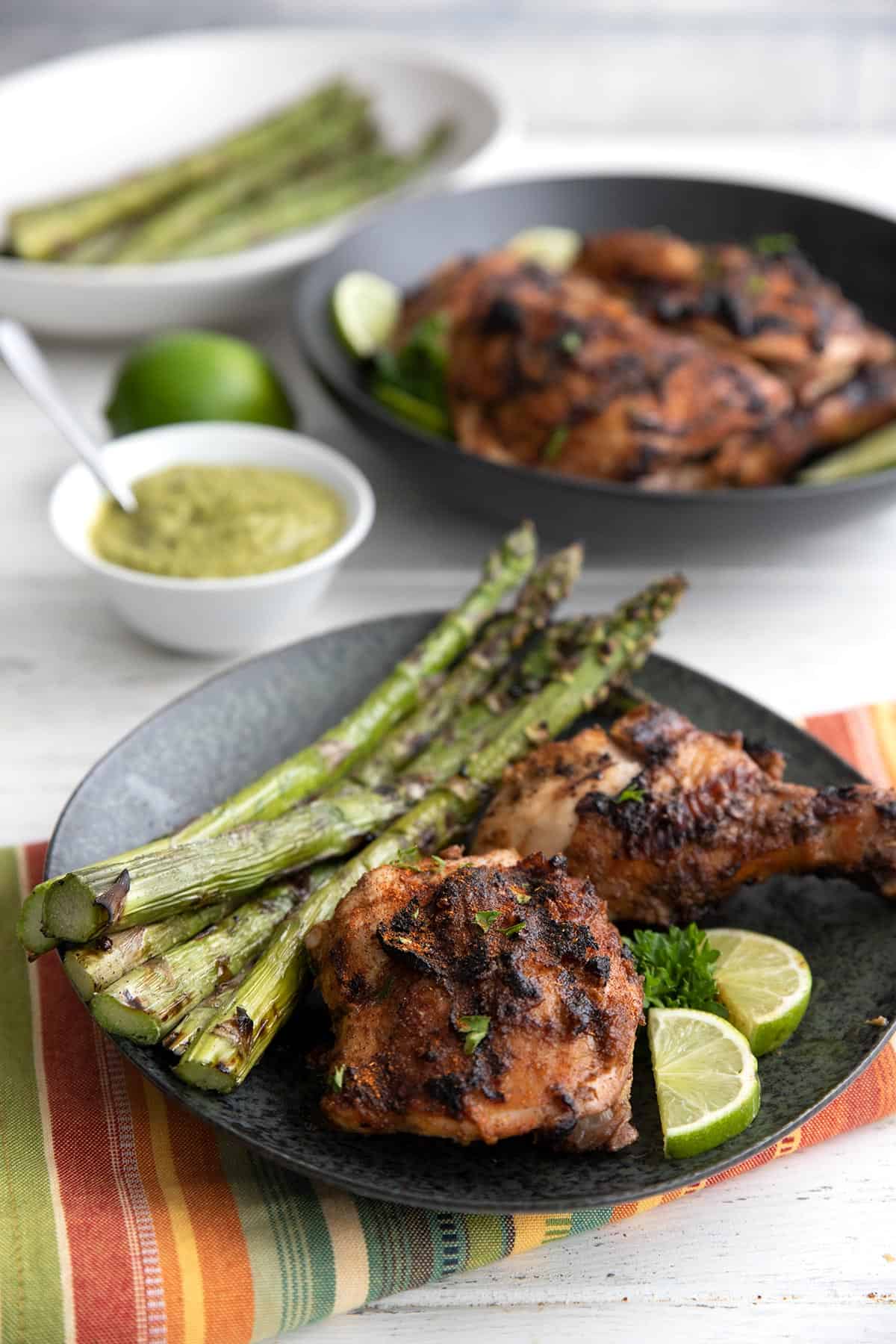 A black plate with two pieces of Peruvian Chicken, as well as grilled asparagus.