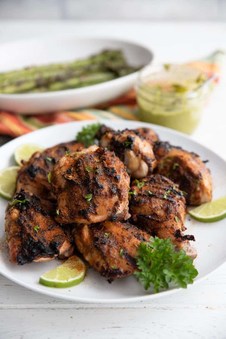 A white bowl full of grilled Peruvian chicken with a jar of creamy cilantro sauce in the background.