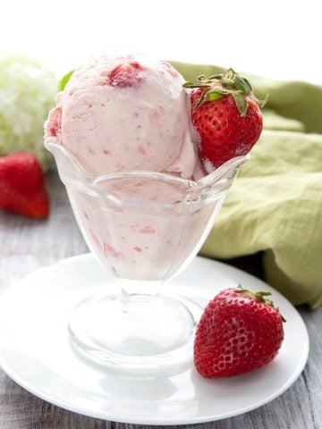 Keto strawberry ice cream in a glass dish in front of a green napkin.