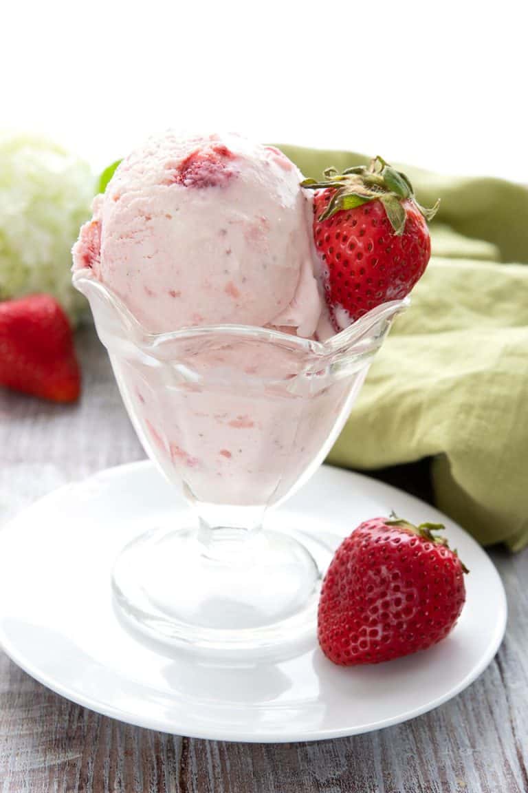 Keto strawberry ice cream in a glass dish in front of a green napkin.