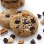 Close up shot of two keto chocolate chip cookies with chocolate chips and chopped nuts strewn around.