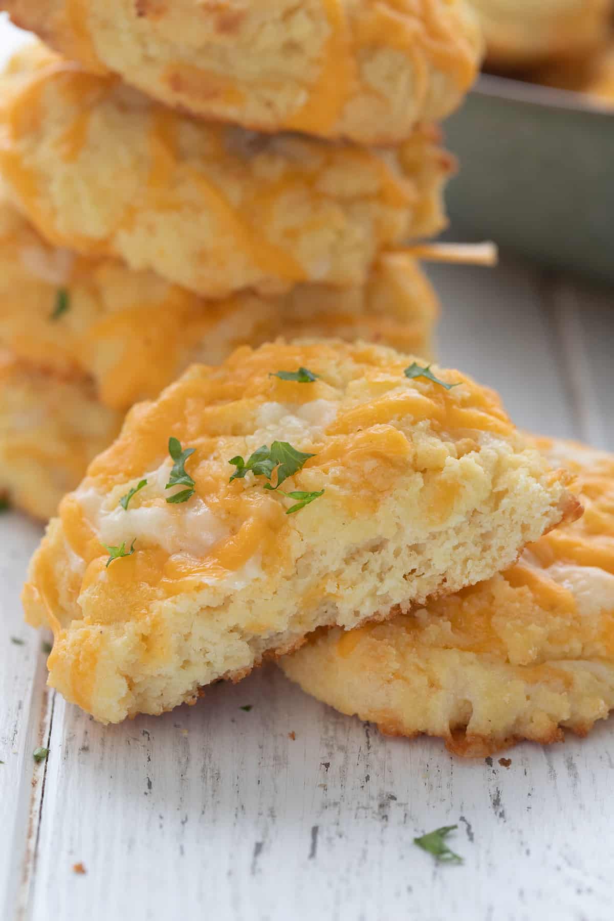 Close up shot of a keto cheddar biscuit broken in half on a white table.