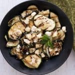 Top down image of perfectly grilled zucchini in a black bowl, topped with feta.