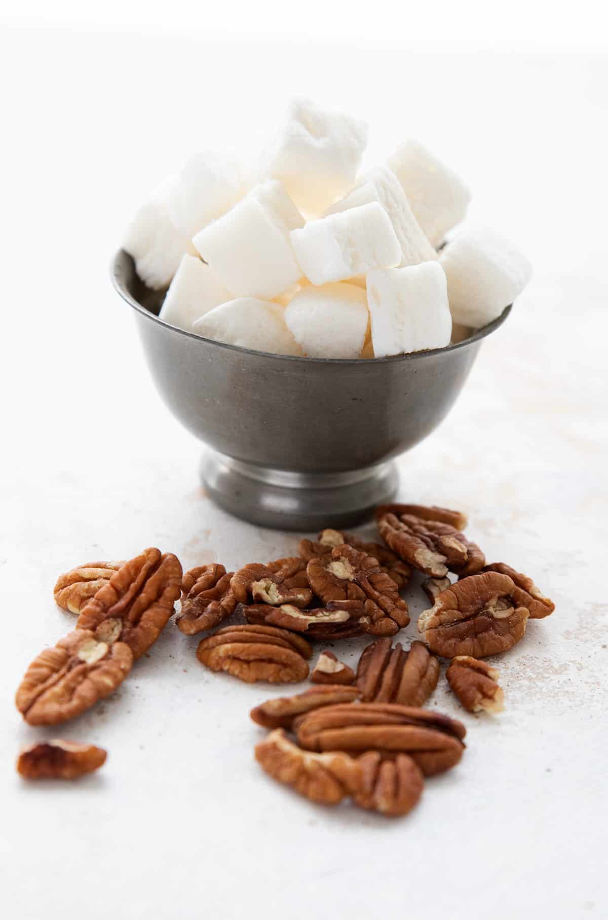 Keto marshmallows in a bowl, with pecans strewn around in front.
