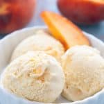 Keto peach ice cream in a white bowl with a slice of peach.