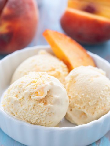 Keto peach ice cream in a white bowl with a slice of peach.