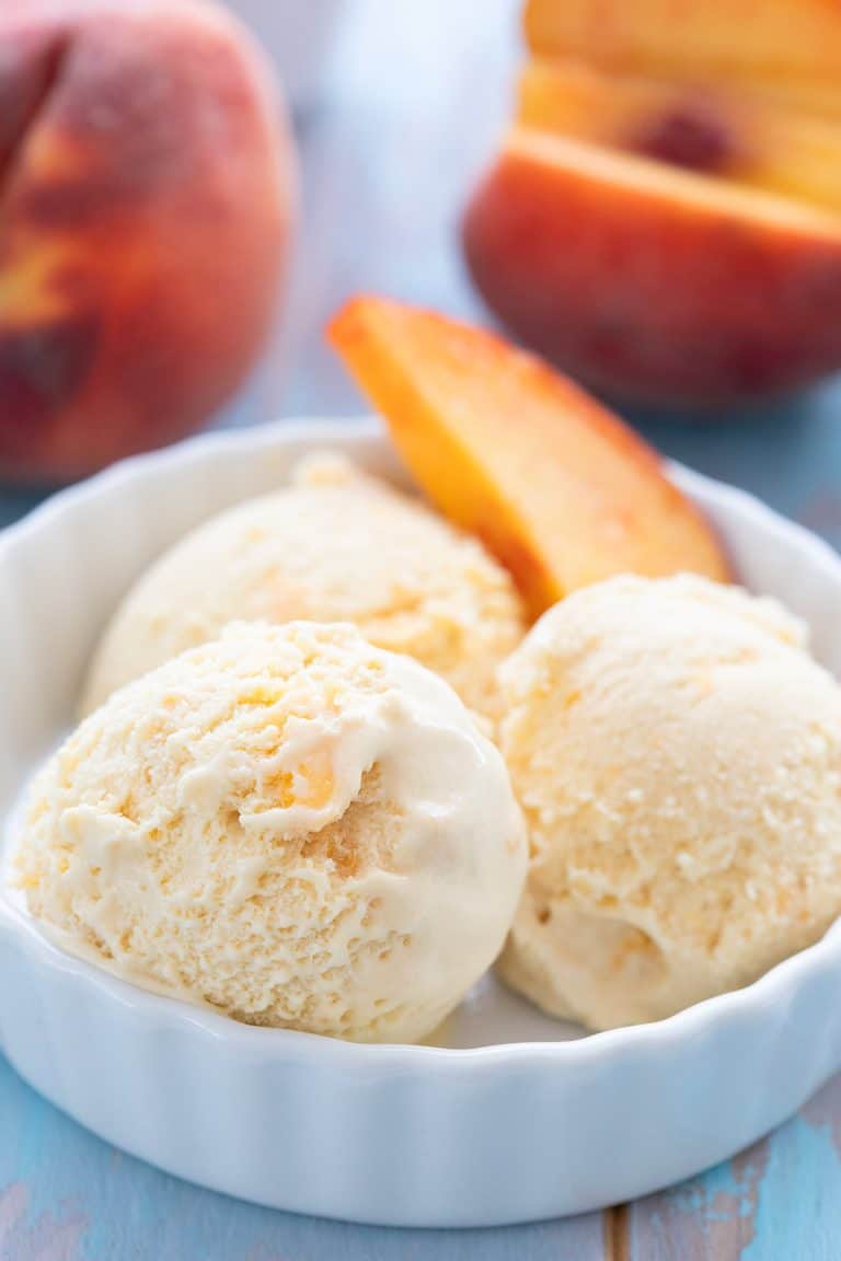 Keto peach ice cream in a white bowl with a slice of peach.