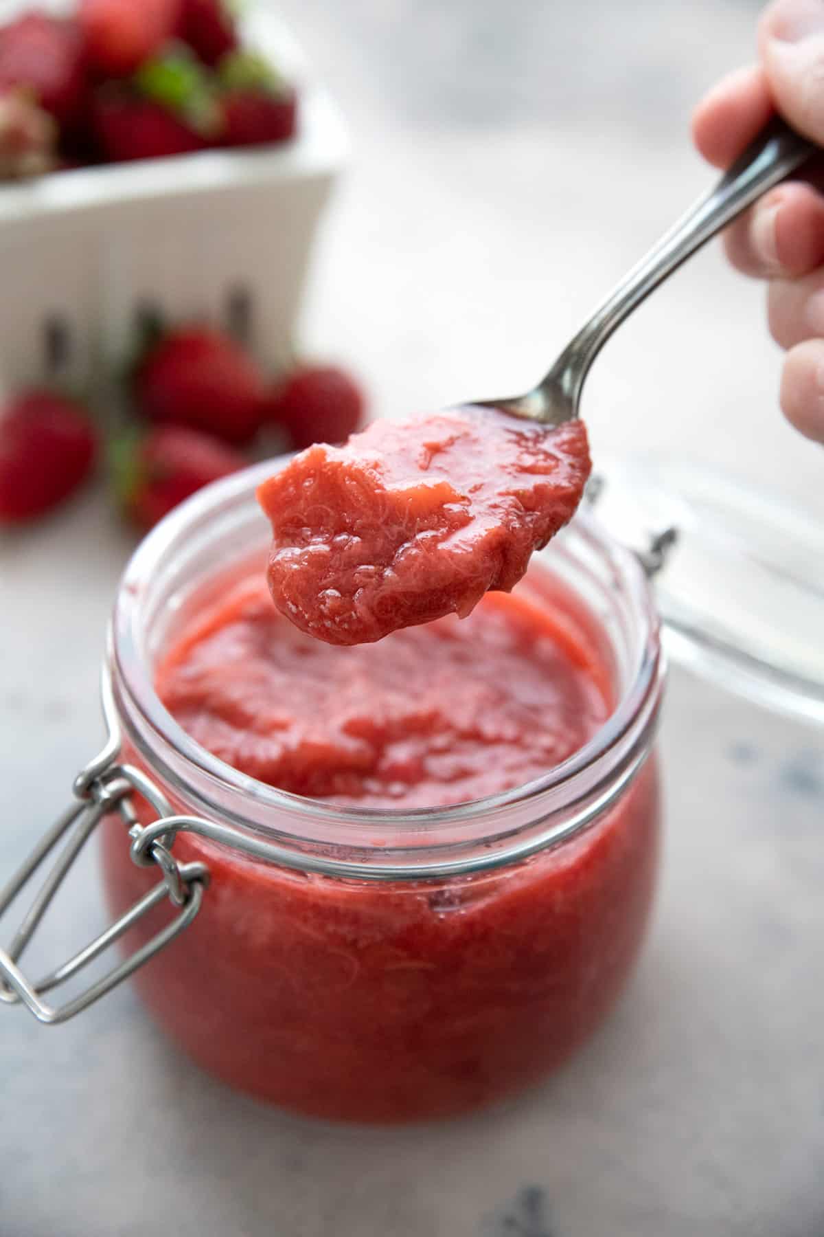A spoon digging into a jar of strawberry rhubarb sauce.