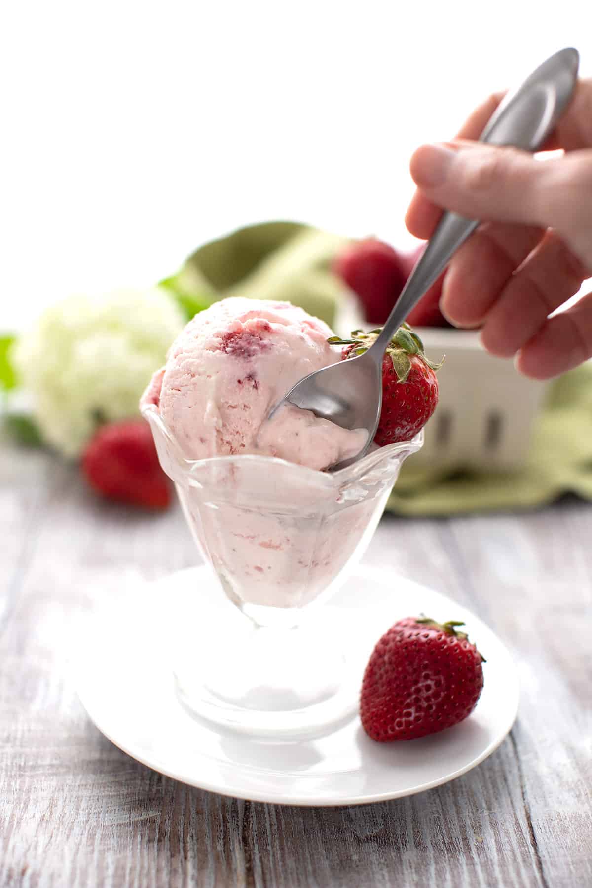 A hand reaching in with a spoon for a bite of strawberry ice cream.