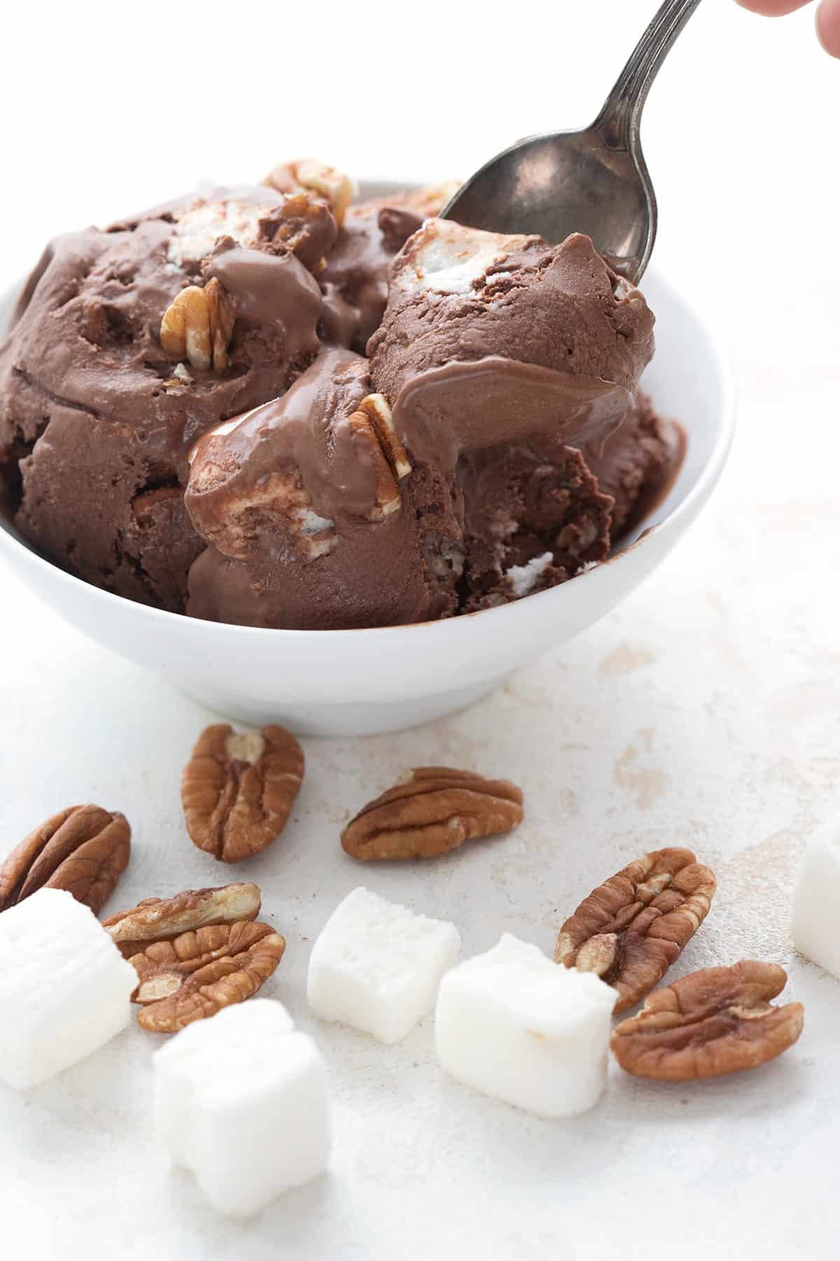 A bowl of keto rocky road ice cream with keto marshmallows and pecans in front.
