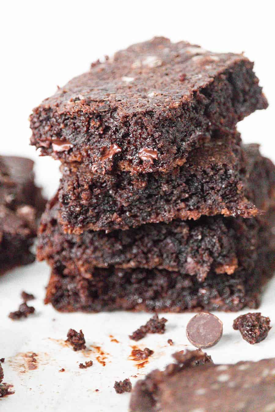 A stack of fudgy keto brownies with crumbs and chocolate chips strewn around.