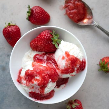 Top down image of keto strawberry rhubarb sauce over ice cream, with strawberries strewn around.