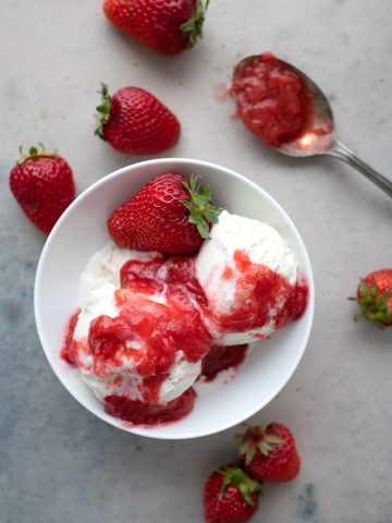 Top down image of keto strawberry rhubarb sauce over ice cream, with strawberries strewn around.