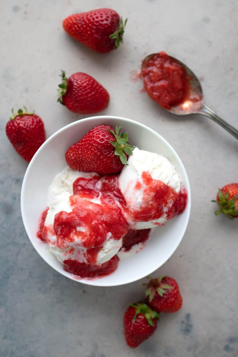 Top down image of keto strawberry rhubarb sauce over ice cream, with strawberries strewn around.