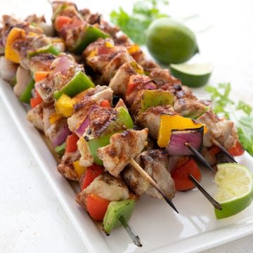 A platter full of freshly grilled keto chicken skewers, with lime and cilantro in the background.