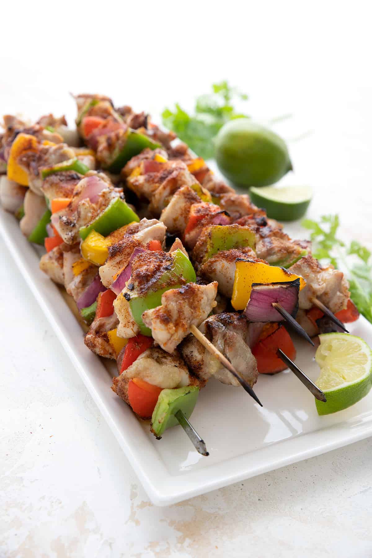A platter full of freshly grilled keto chicken skewers, with lime and cilantro in the background.