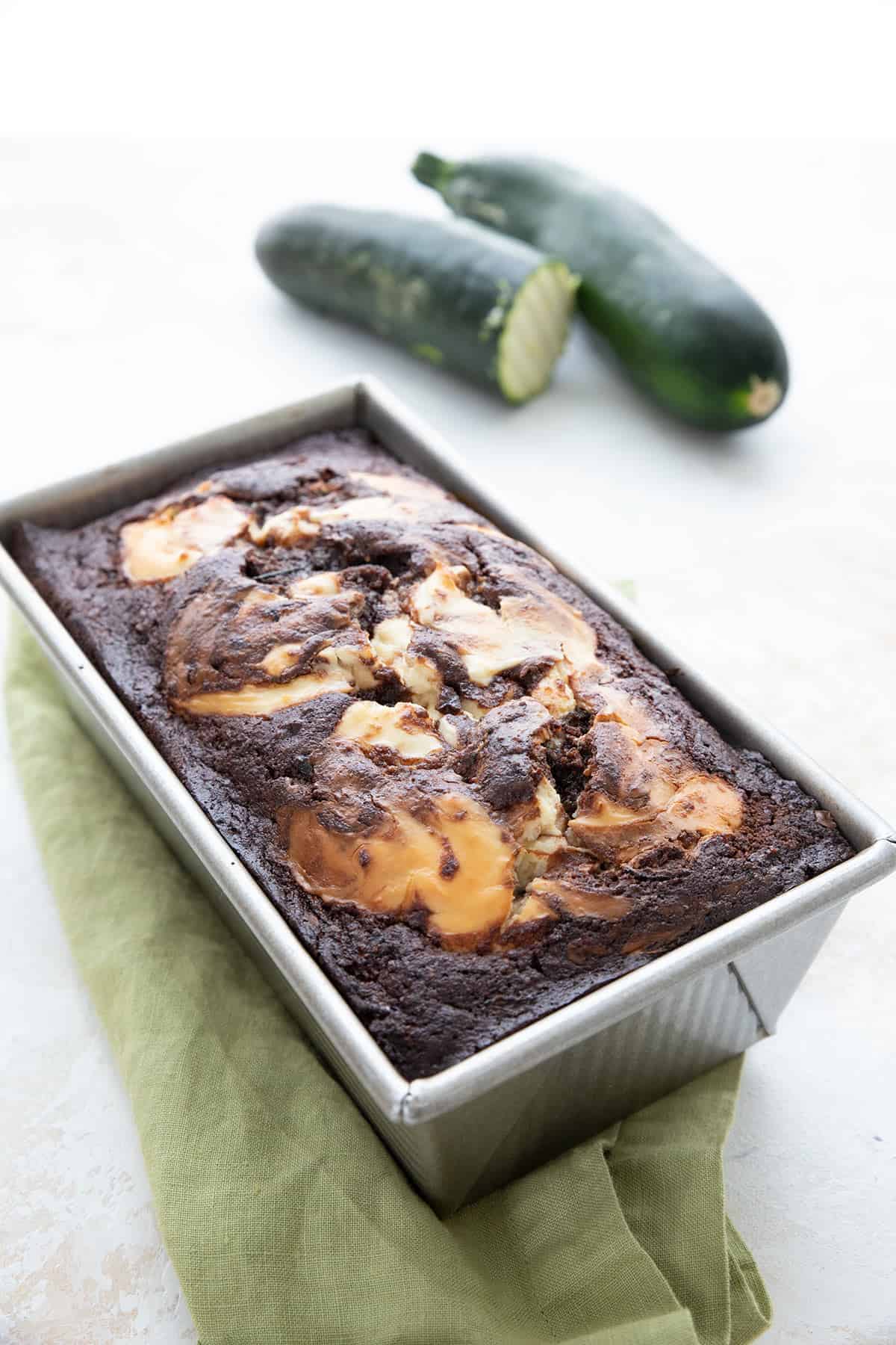Keto Chocolate Cream Cheese Zucchini bread in the loaf pan with zucchini in the background.