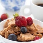 Titled image of a white bowl of Keto Cinnamon Crunch Cereal over a blue patterned napkin.