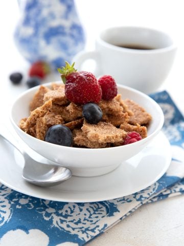 A white bowl filled with keto cereal, topped with fresh berries, over a blue patterned napkin.