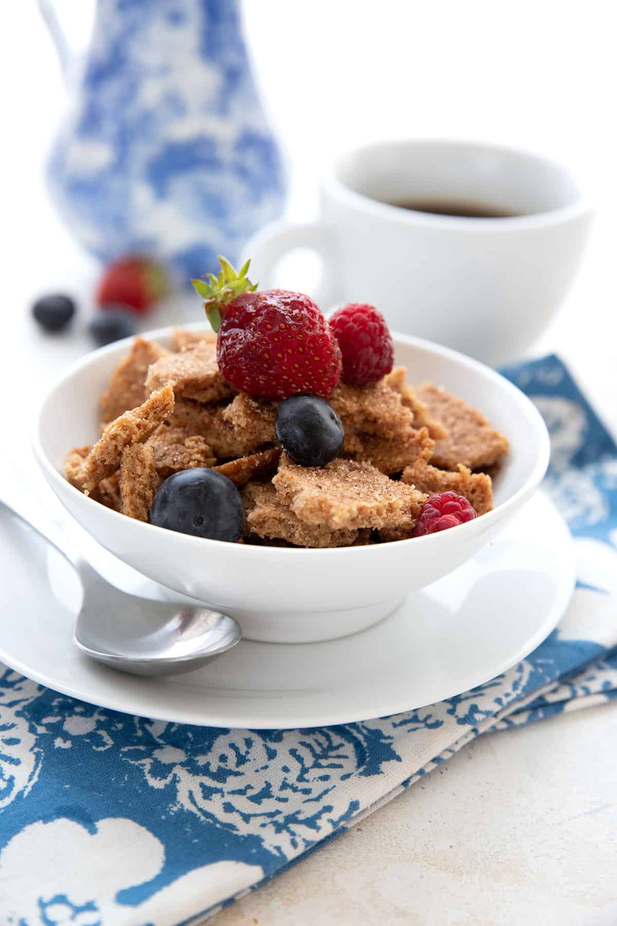 A white bowl filled with keto cereal, topped with fresh berries, over a blue patterned napkin.