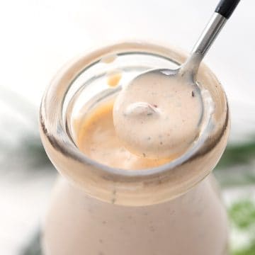 Close up of a spoon lifting some Chipotle Ranch Dressing out of a glass bottle.