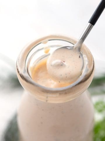 Close up of a spoon lifting some Chipotle Ranch Dressing out of a glass bottle.