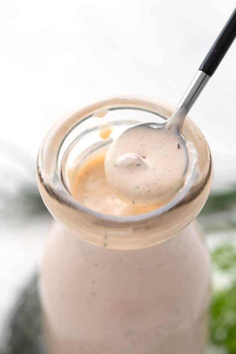 Close up of a spoon lifting some Chipotle Ranch Dressing out of a glass bottle.