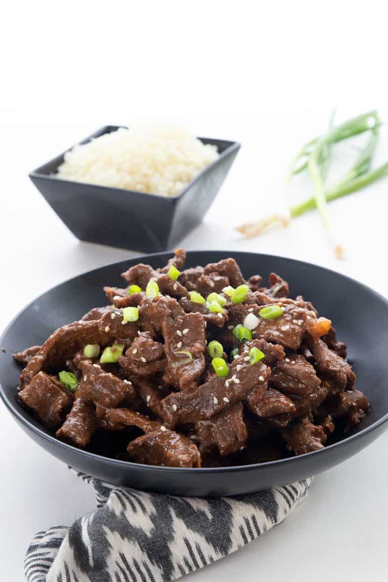 Keto Mongolian Beef in a large bowl with cauliflower rice and green onion in the background.