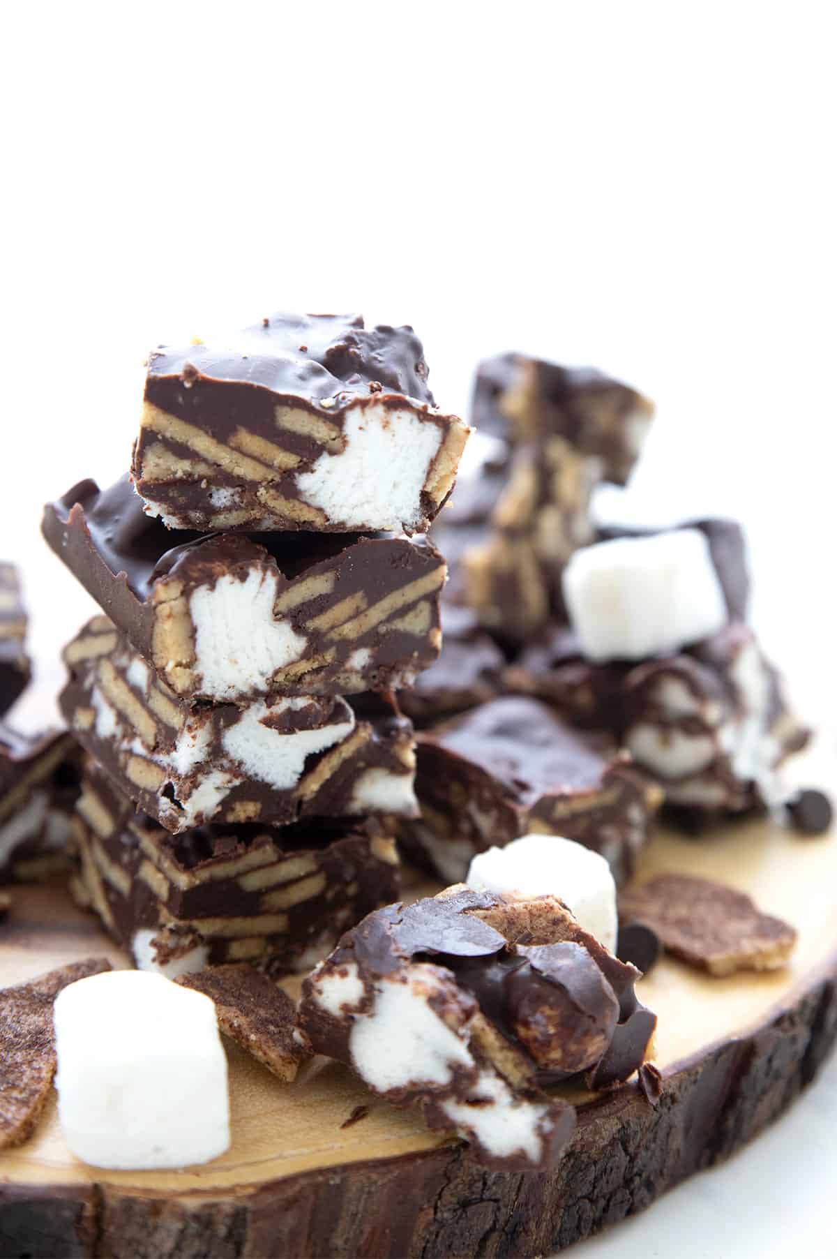 A stack of Keto Smores Bites on a wooden platter with marshmallows and keto crackers strewn around. 