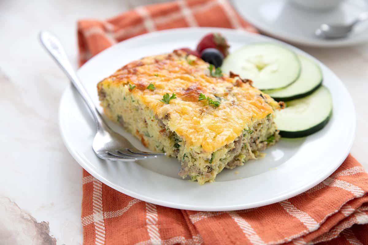 A slice of Keto Breakfast Casserole on a white plate with cucumbers and berries.