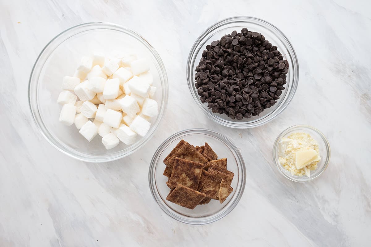 Top down image of keto chocolate chips, keto crackers, keto marshmallows and butter in glass bowls. 