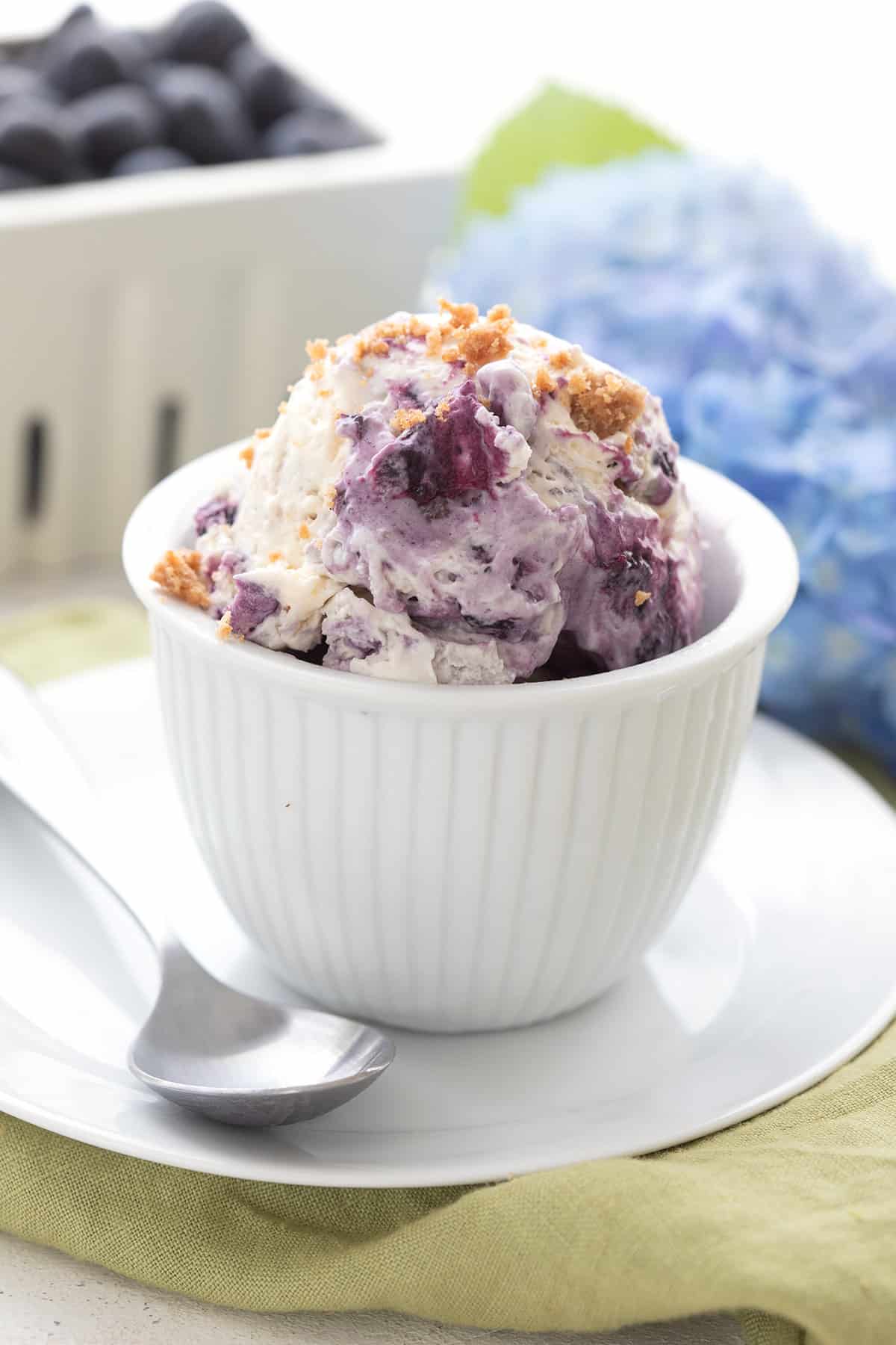 Keto Blueberry Ice Cream in a white dish over a green napkin, with blue hydrangeas in the background.