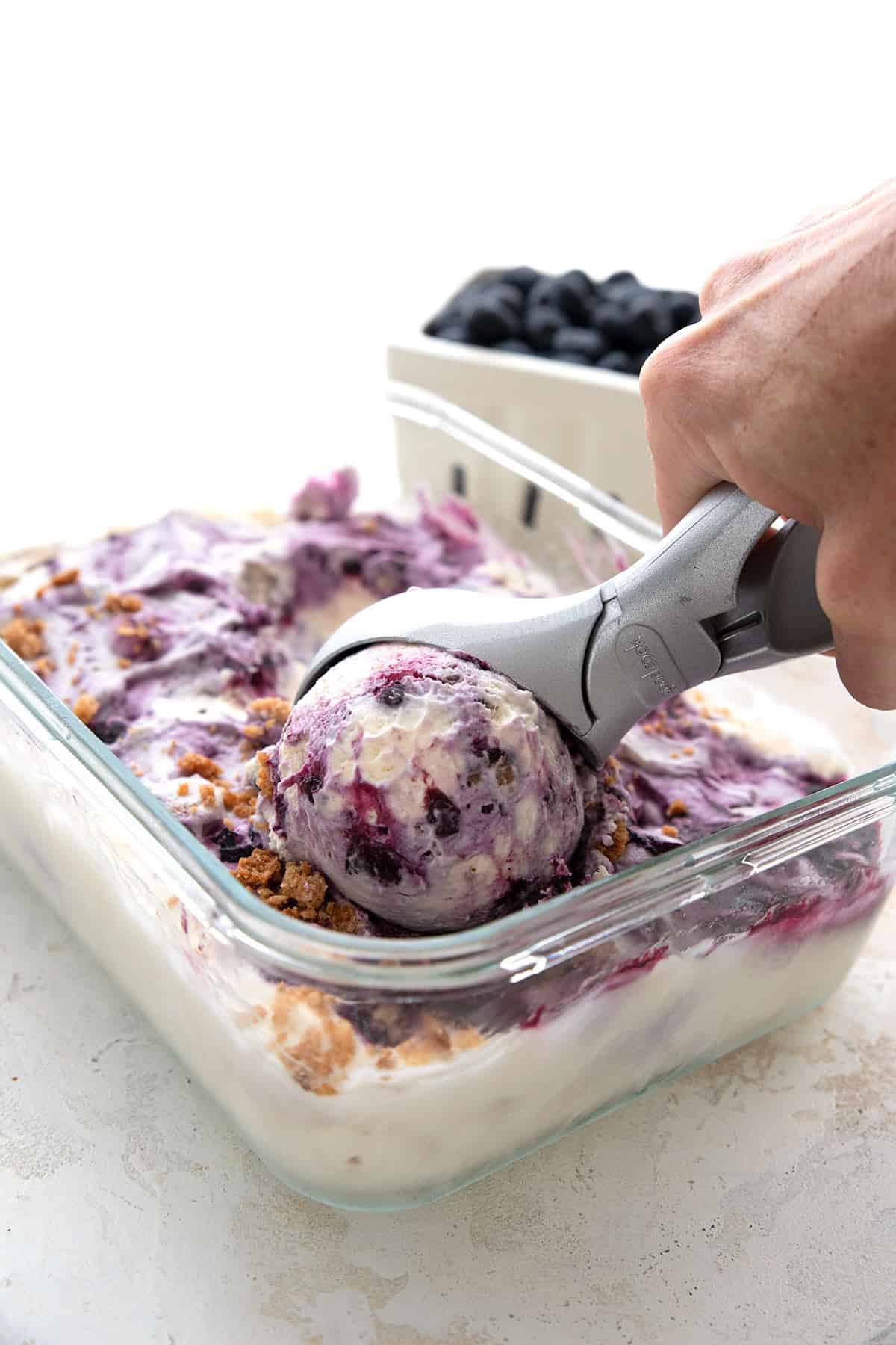 A ice cream scoop scooping blueberry pie ice cream out of the freezer container.