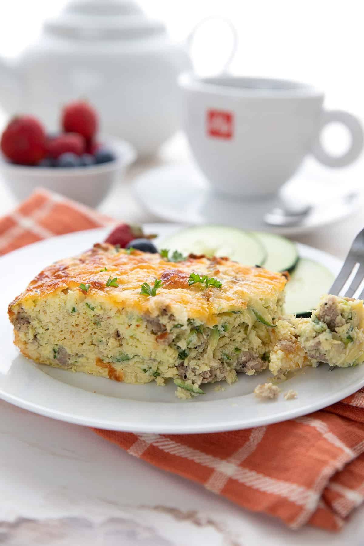A slice of zucchini sausage breakfast casserole on a white plate with a forkful taken out of it.