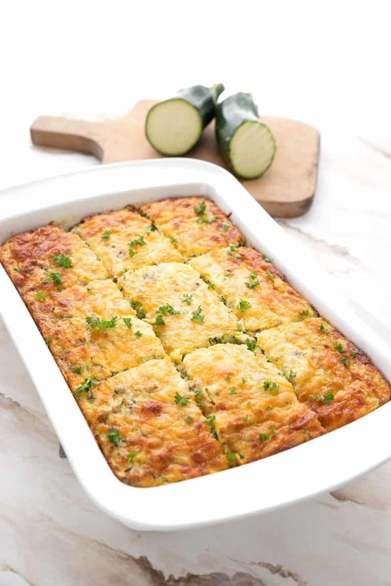 Keto Zucchini Breakfast Casserole in a white baking dish, with zucchini the background.