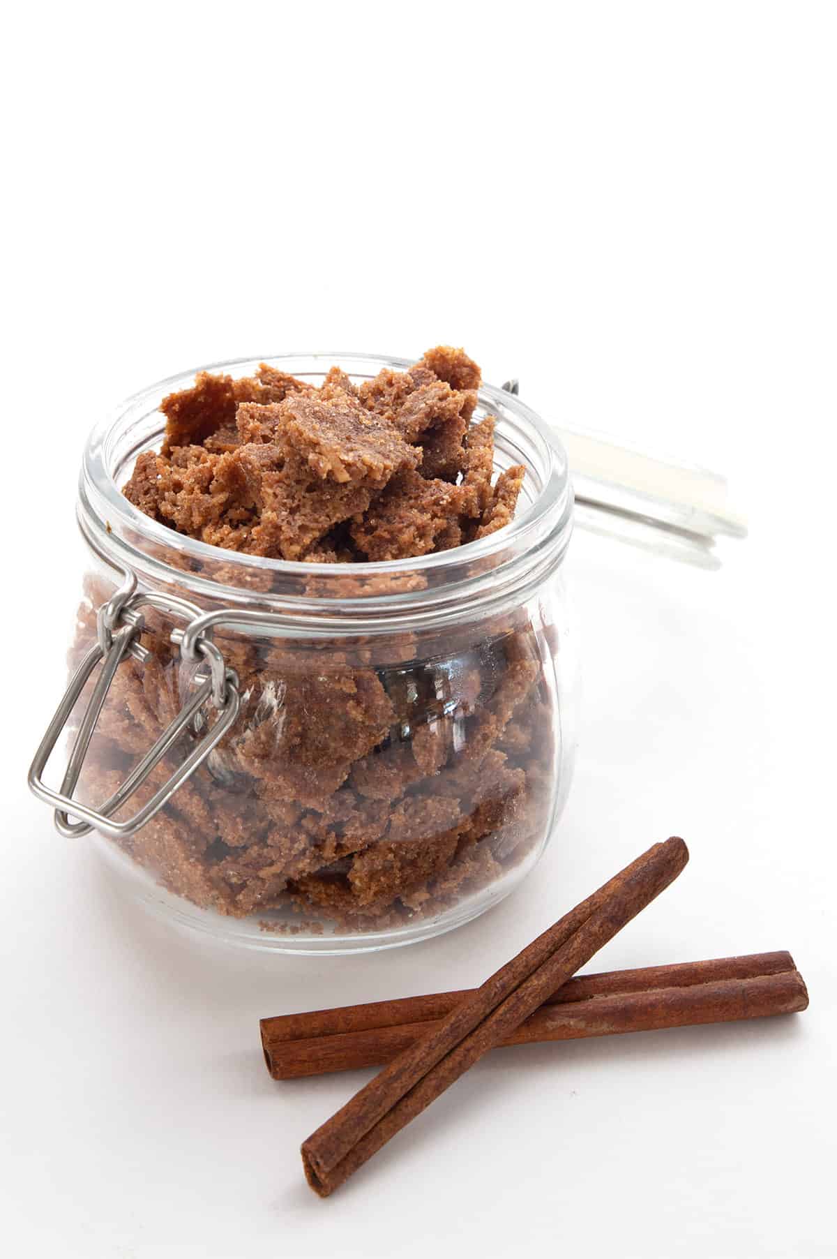 Cinnamon Crunch Keto Cereal in a big glass jar with two cinnamon sticks in front.