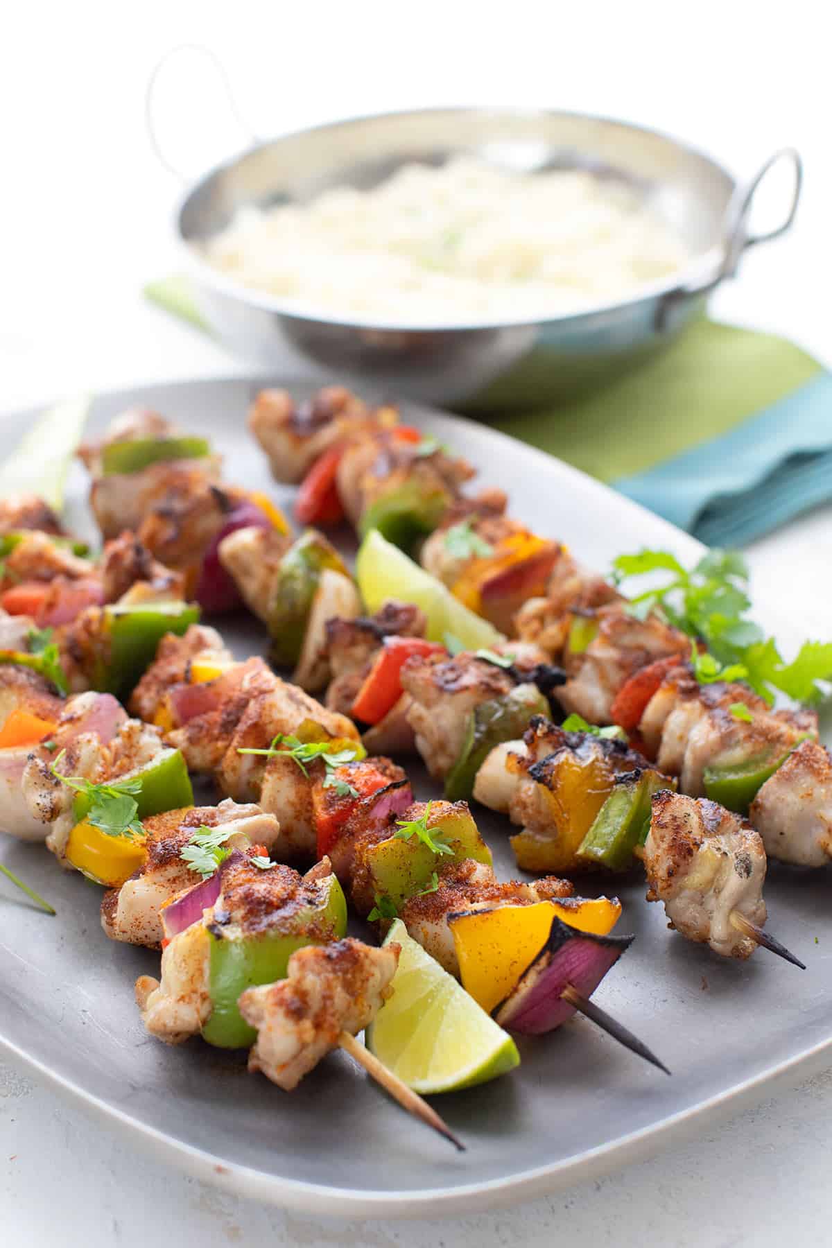 A metal plate with four chicken fajita skewers and lime wedges.