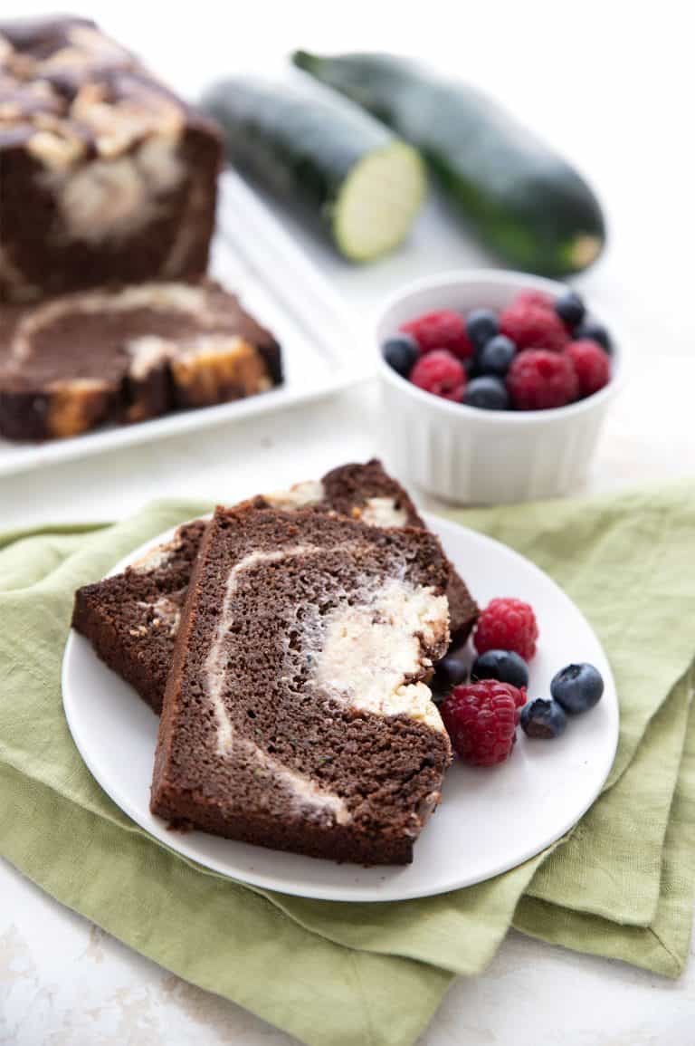 Two slices of keto chocolate zucchini bread on a white plate with berries.