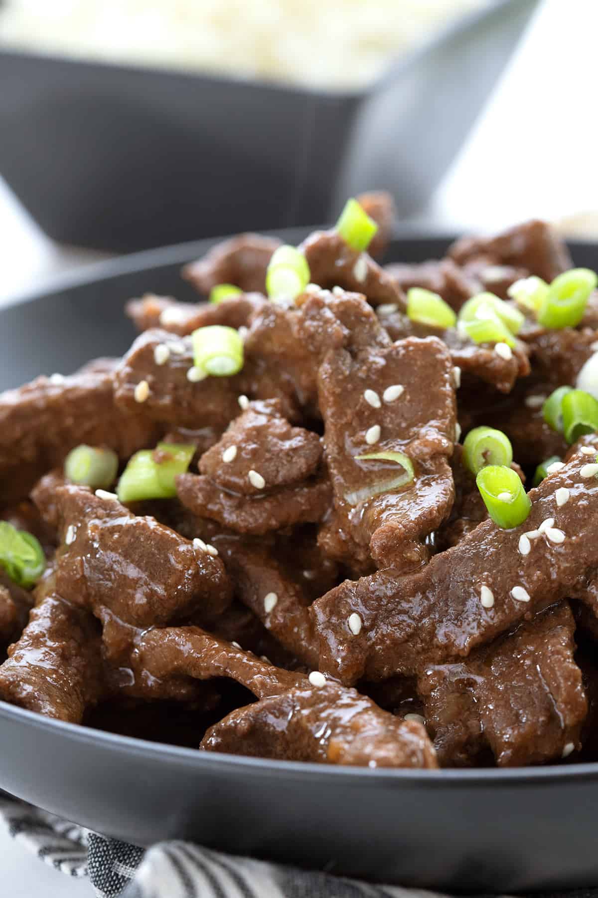 Close up shot of keto Mongolian beef in a black bowl, with sesame seeds and green onion.