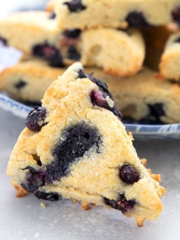 A blueberry keto scones in front of a plate of more scones on a gray table.