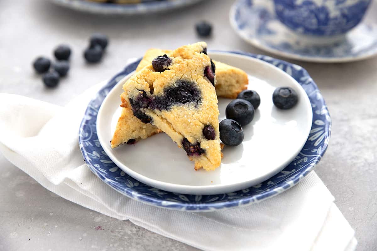 Two keto scones on a white plate with blueberries, over a white napkin.