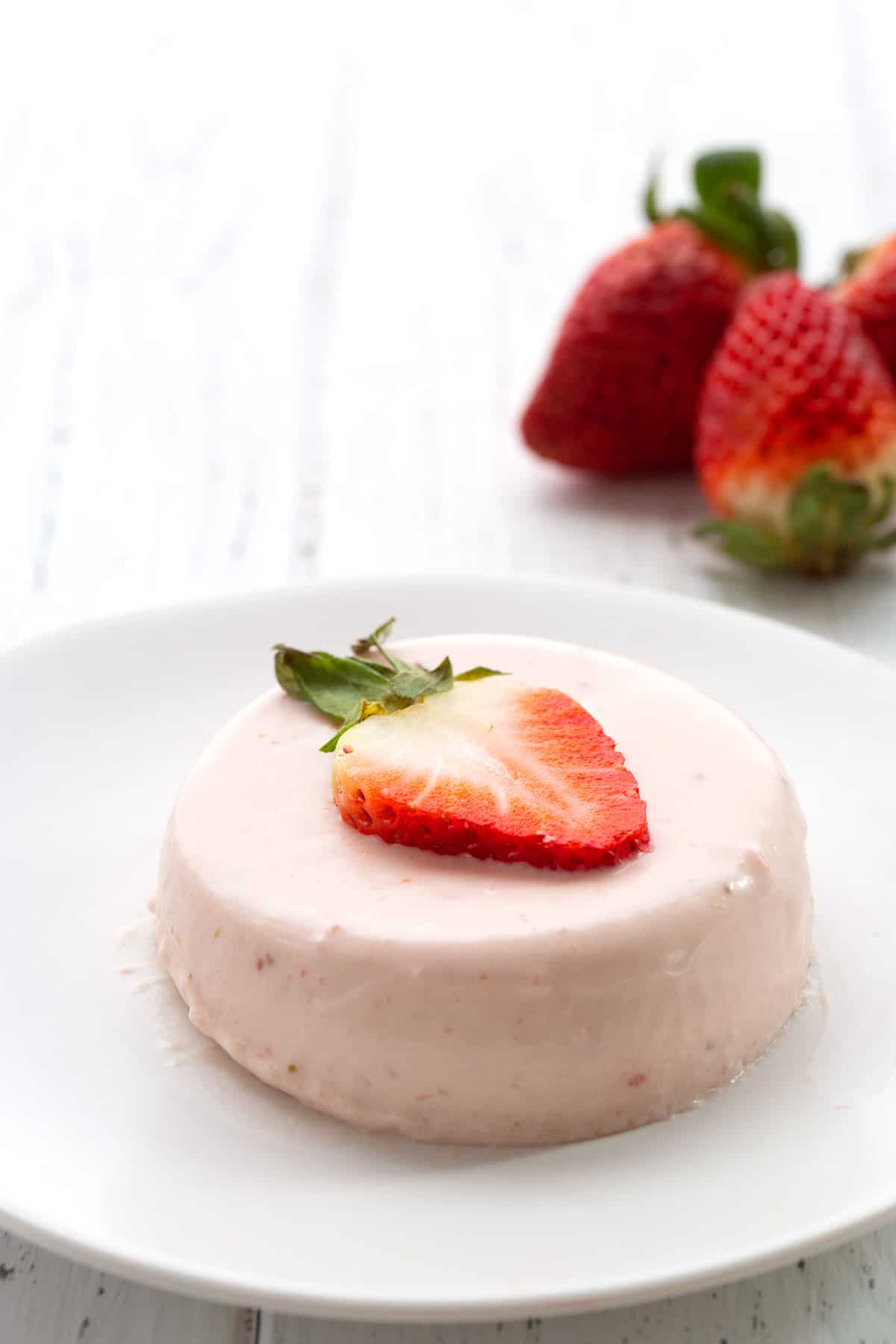 A white plate with keto panna cotta and a sliced strawberry.